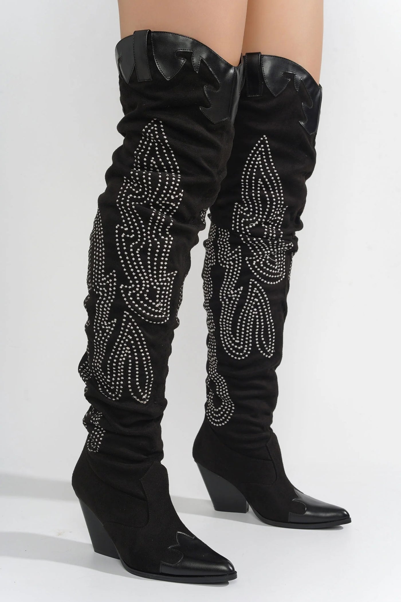 Detailed view of black cowboy boots reaching above the knee, adorned with tonal embroidery in a Western-inspired pattern, highlighting the pointed toe and unique design