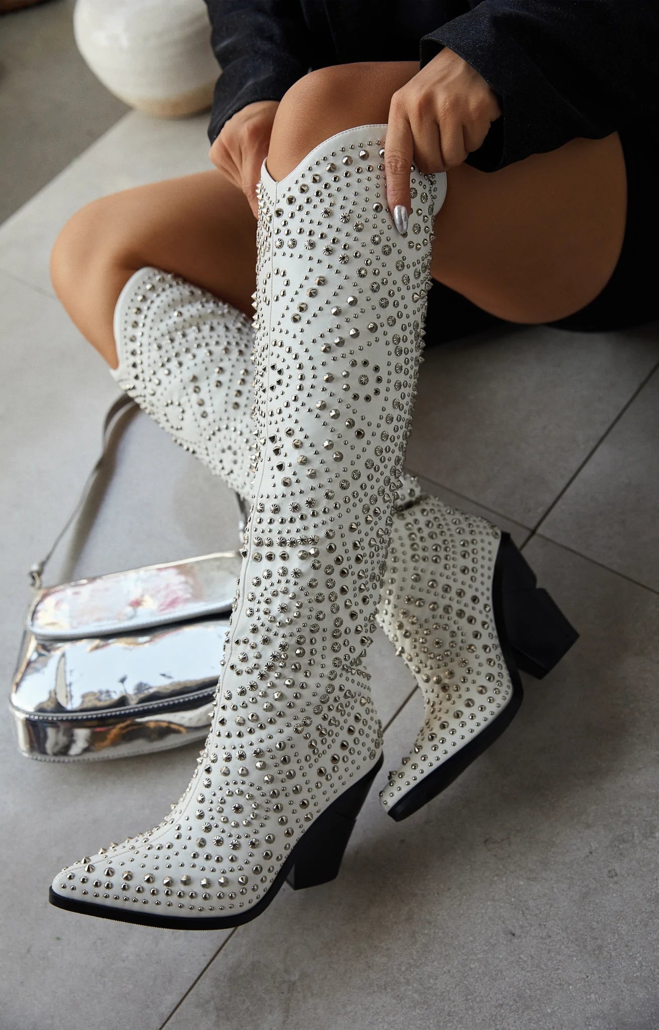 White cowboy boots with a pointed toe and block heel, embellished with silver studs and rhinestones in a detailed pattern