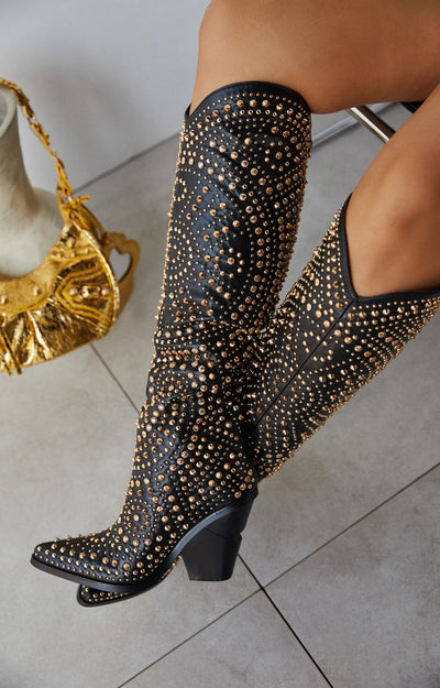 Black cowboy boots with a pointed toe and block heel, embellished with gold studs and rhinestones in a detailed pattern