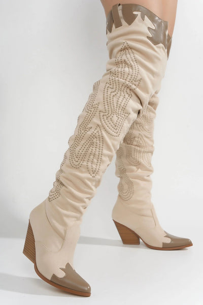 Detailed view of beige cowboy boots reaching above the knee, adorned with tonal embroidery in a Western-inspired pattern, highlighting the pointed toe and unique design