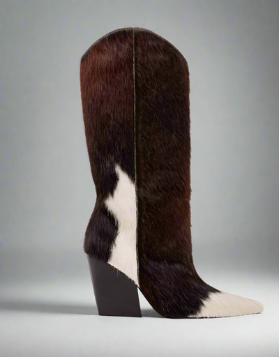 Cowboy boot with a unique patchwork design of brown and white cowhide fur, featuring a pointed toe, high shaft, and chunky black heel.